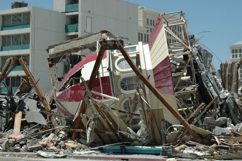 Daylight demolition photo: a red-and-white striped cupola from the Boardwalk facade lies crushed sideways in a pile of twisted steel and concrete rubble, with Bellagio's tower in the background.
