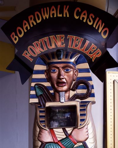 Egyptian-style fortune teller automaton beneath an arched black sign reading Boardwalk Casino Fortune Teller in yellow-to-red carnival lettering.