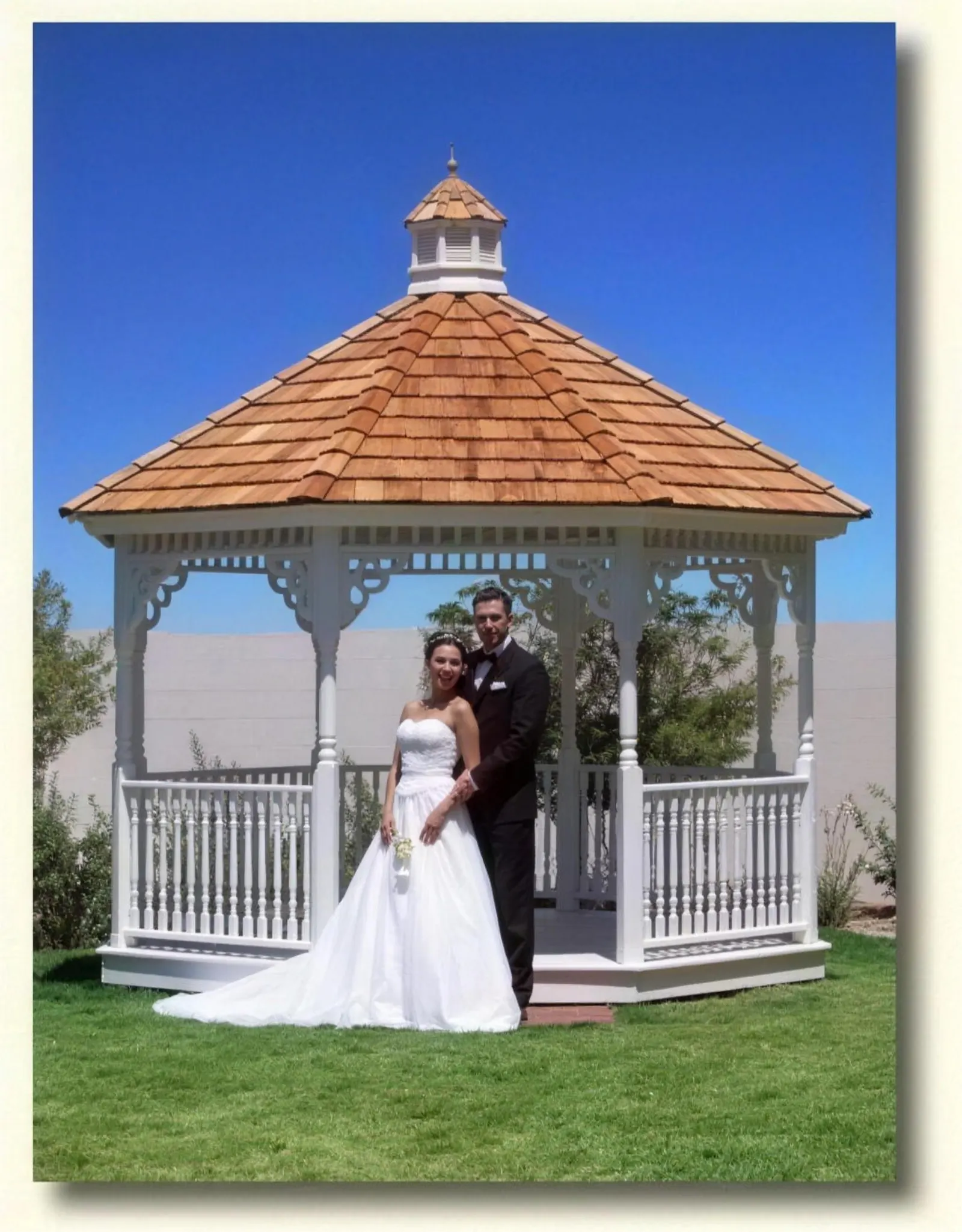 A newlywed couple standing beneath the Boardwalk&rsquo;s white octagonal wedding gazebo under a bright blue sky.