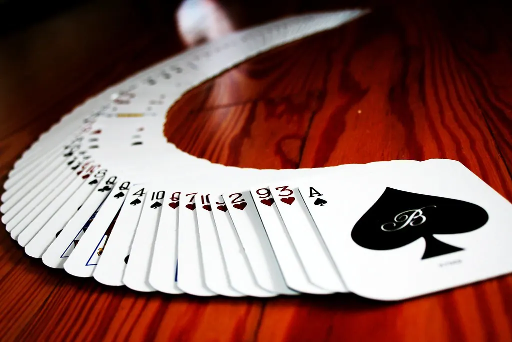 Souvenir playing cards fanned across a wooden table with a black spade card on top.
