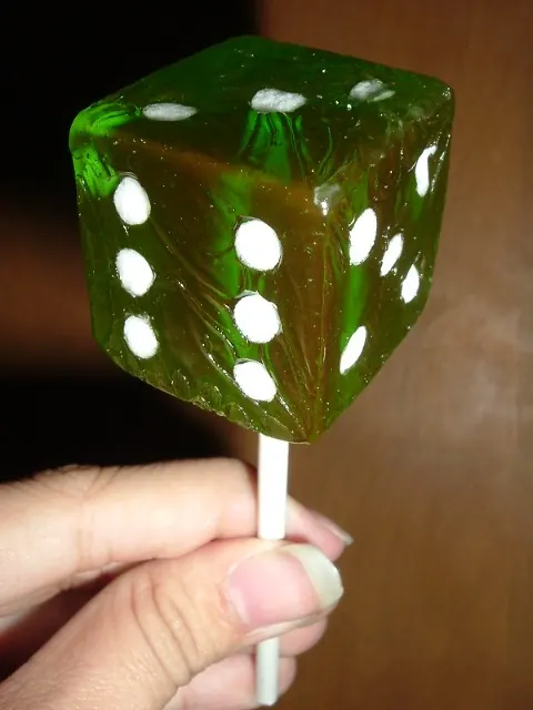 Green translucent dice-shaped novelty lollipop on a white stick.