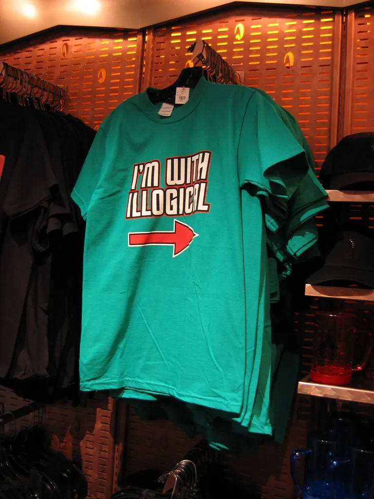 Green novelty T-shirt on a gift-shop rack reading I'm with illogical with an arrow.
