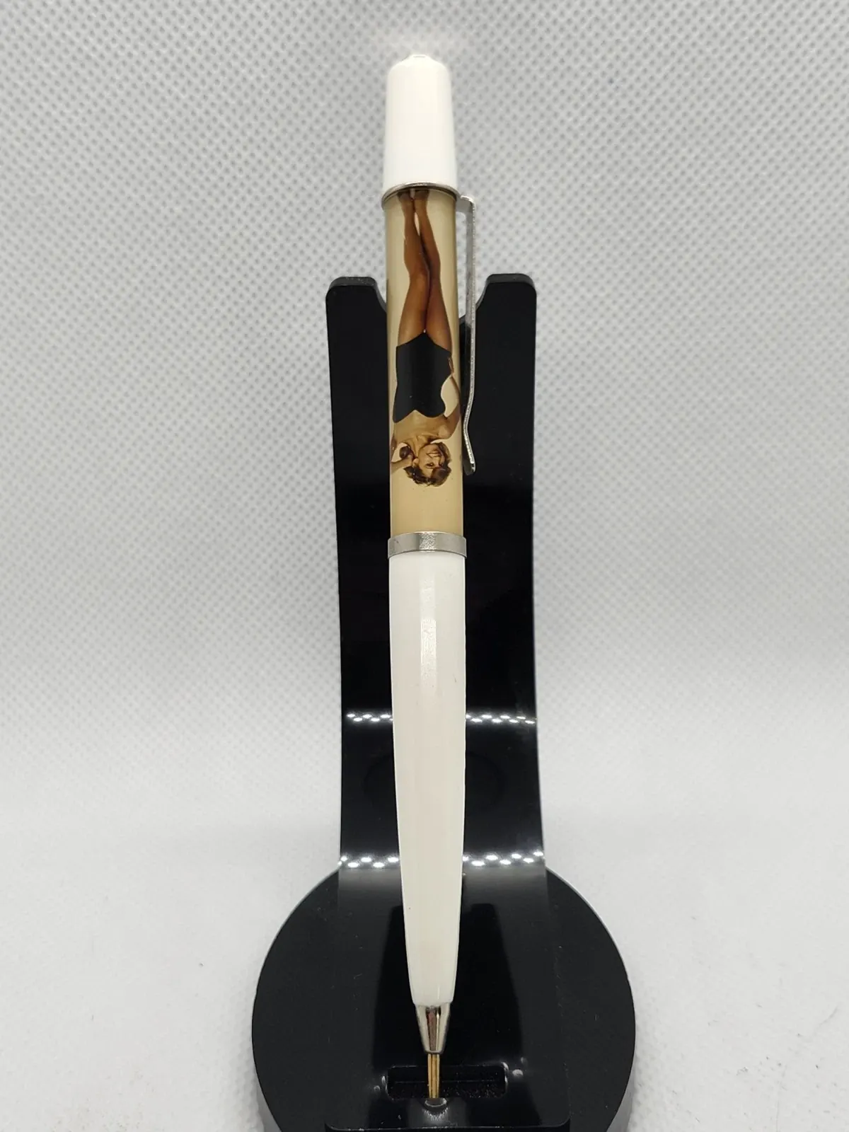 White vintage floating-image novelty pen displaying a pin-up woman, standing upright in a black display holder.