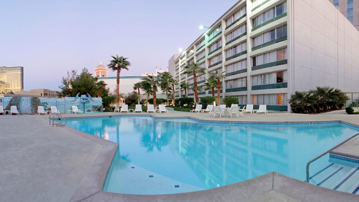 Upscaled wide view of the Boardwalk pool, painted waterfall wall, palms and six-story hotel wing.