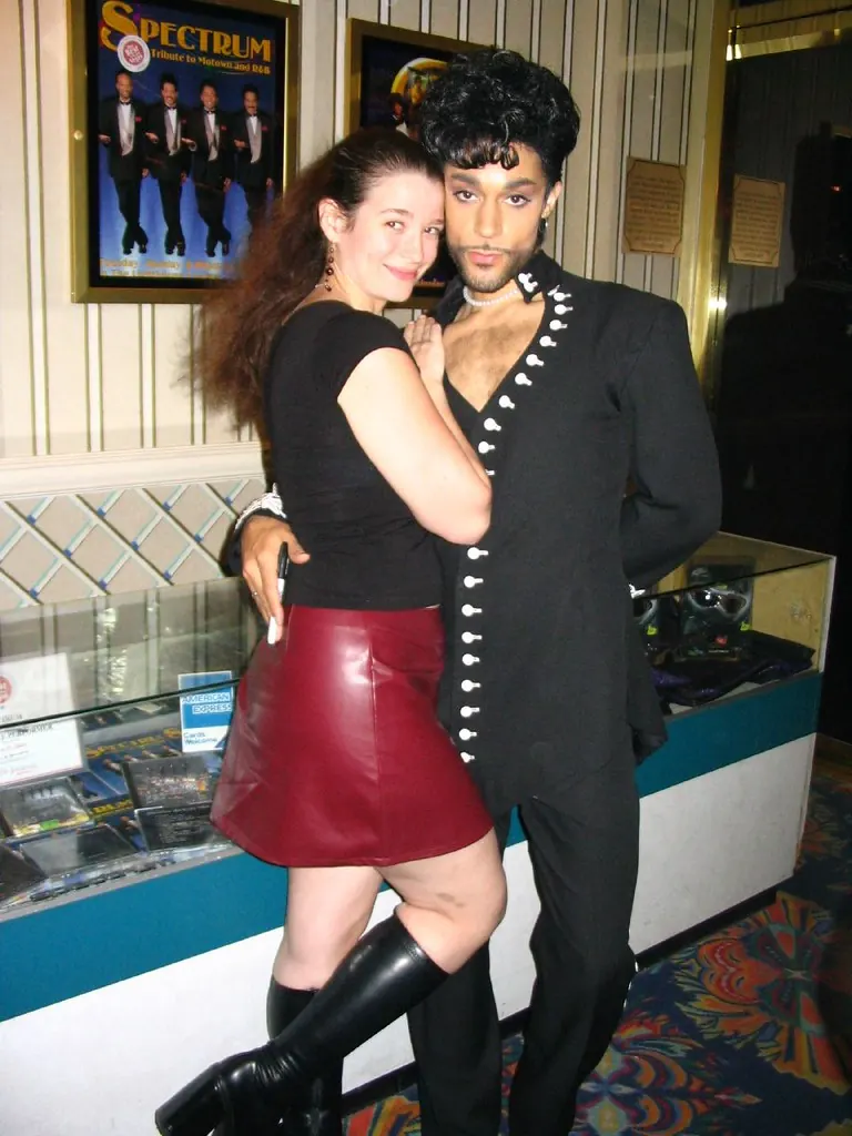 A visitor poses with the Purple Reign performer in the Boardwalk lounge lobby; the Spectrum poster and patterned carpet appear behind them.