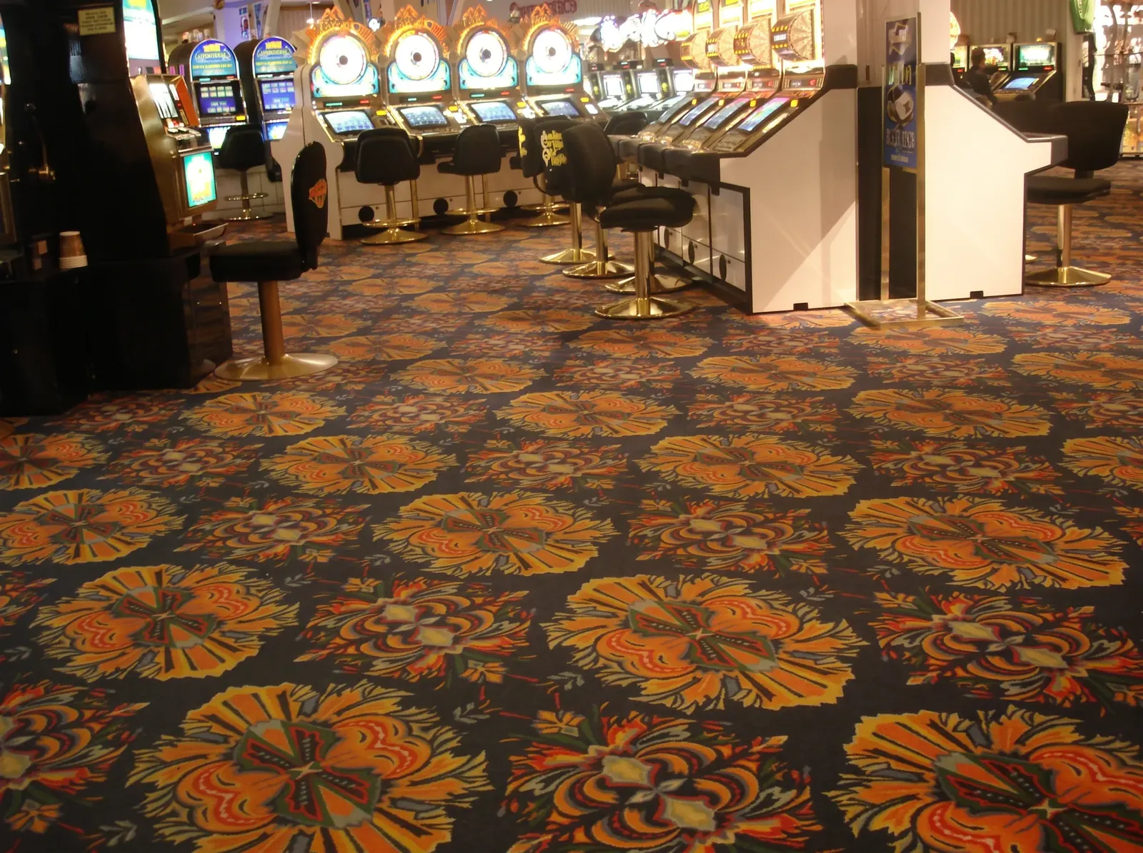 The Boardwalk casino floor's dark carpet covered in enormous orange and gold firework medallions, with rows of slot machines beyond.