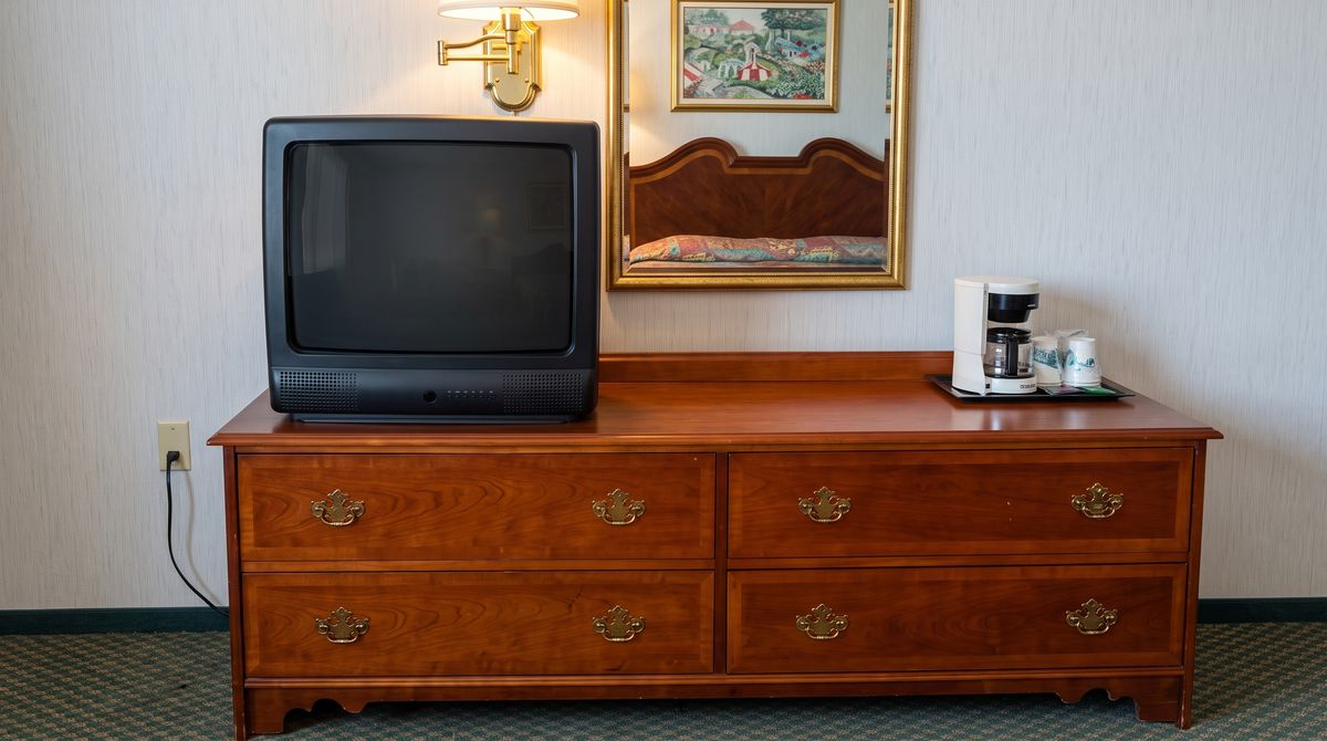 The room's cherry dresser with a tube television, a four-cup coffee maker with wrapped cups on a tray, and a gold-framed mirror reflecting one of the beds.