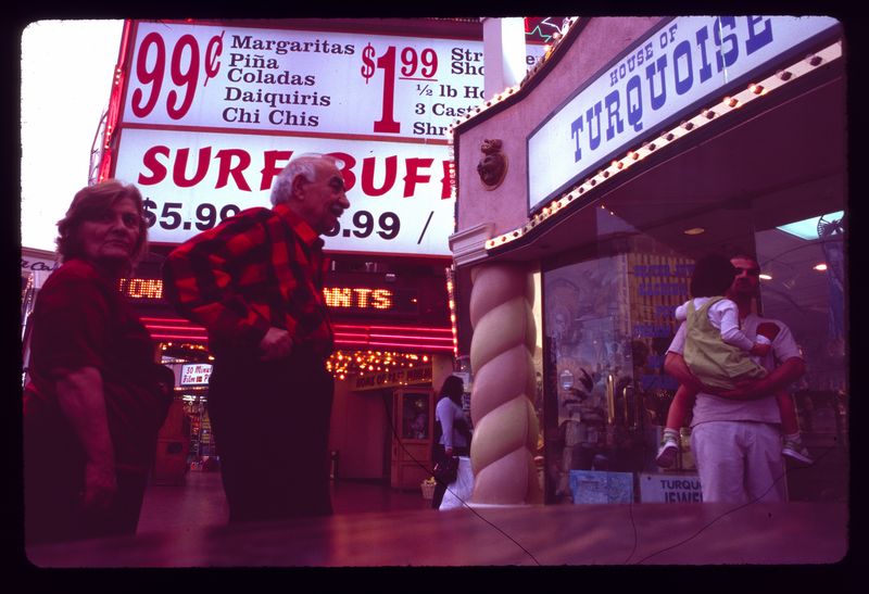 November 2000 Ektachrome photograph at the Surf Buffet entrance: large illuminated panels advertise 99-cent cocktails, $1.99 food specials and the buffet at $5.99; pedestrians pass the neighboring House of Turquoise shop.