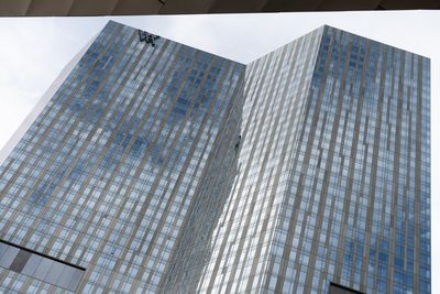Looking up at the Waldorf Astoria Las Vegas: a tall blue-glass tower with a small Waldorf Astoria monogram near the top, reflecting an overcast sky.